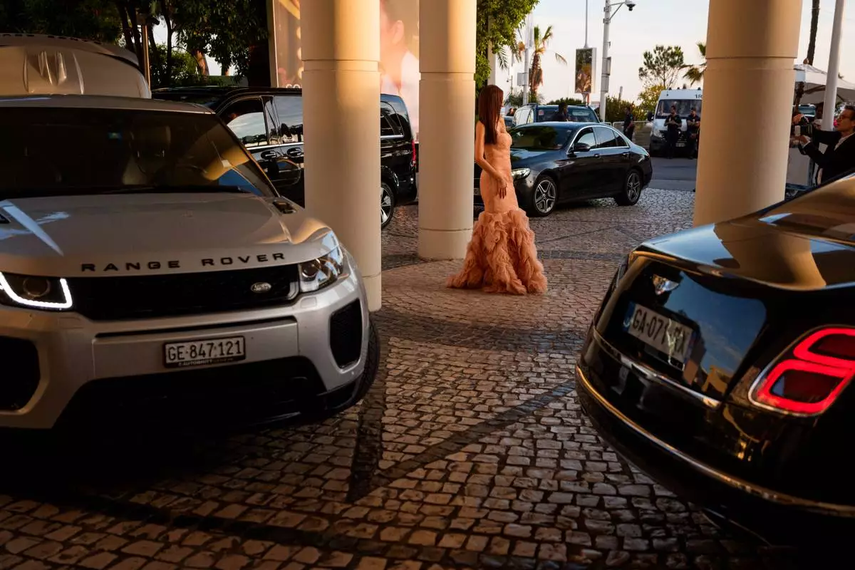 A woman poses for a photographer in the parking lot of Hotel Martinez as cars line up to take festivalgoers to the 79th international film festival, Cannes, southern France, Tuesday, May 19, 2026. (AP Photo/Andreea Alexandru)