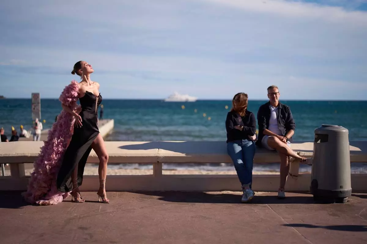 A festivalgoer poses for photographers as people sit by the beach along the Croisette during the 79th international film festival, Cannes, southern France, Friday, May 15, 2026. (AP Photo/John Locher)