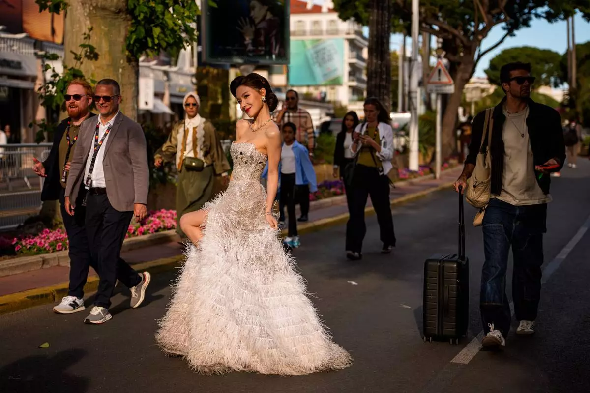 People walk past a woman posing for photographers after walking on the red carpet for the movie "Parallel Talles" during the 79th international film festival, Cannes, southern France, Thursday, May 14, 2026. (AP Photo/Andreea Alexandru)