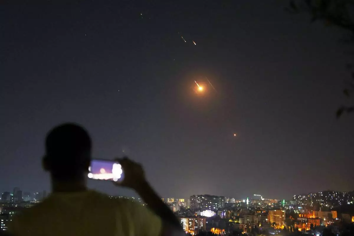 FILE — A man takes a cellphone photo as missiles fired from Iran toward Israel fly over Syrian territory in Damascus, Syria, early Wednesday, June 18, 2025. (AP Photo/Ghaith Alsayed, File)