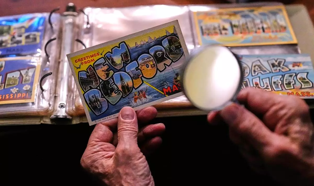 Peter Meggison, a 76-year-old retired community college professor, examines a "New Bedford" postcard from his private collection of more than 10,000 large letter postcards, Monday, May 11, 2026, in Westport, Mass. (AP Photo/Charles Krupa)