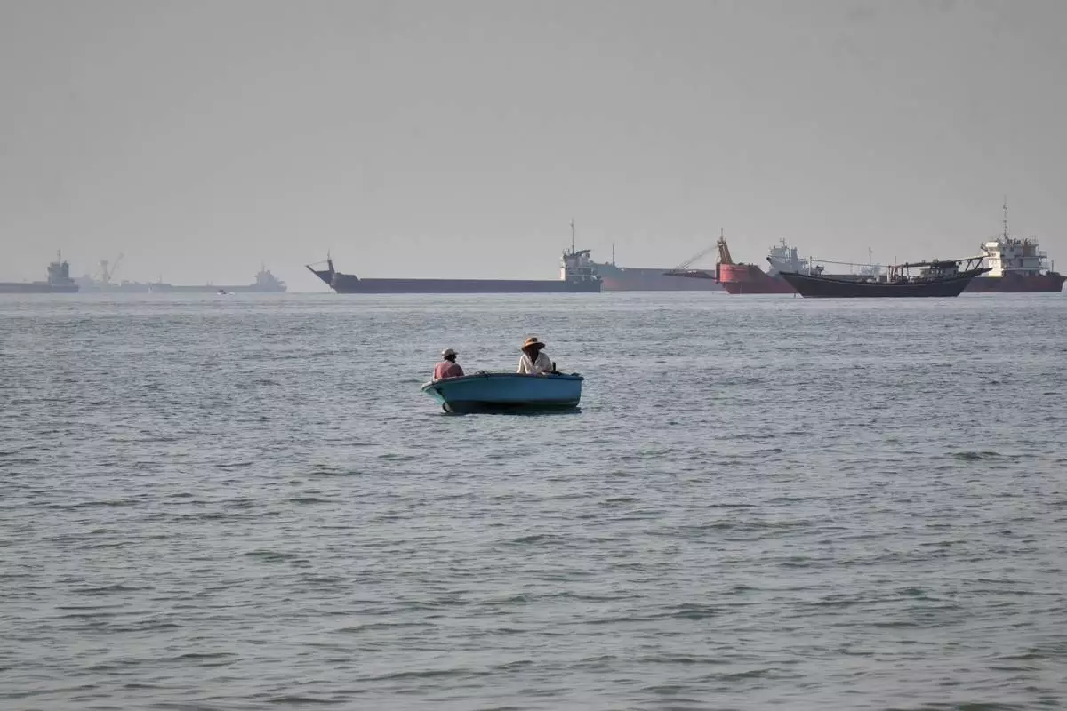 Two men sit in a small boat on the water as a mix of bulk carriers, cargo ships, and service vessels line the horizon in the Strait of Hormuz off Bandar Abbas, Iran, Monday, April 27, 2026.(Razieh Poudat/ISNA via AP)