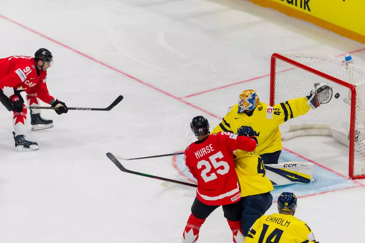 Canada's John Tavares, left, scores against Sweden goaltender Magnus Hellberg, during the 2026 IIHF Men's Ice Hockey World Championship preliminary round group B game between Canada and Sweden, at the BCF Arena ice hockey stadium, in Fribourg, Switzerland, Friday, May 15, 2026. (Salvatore Di Nolfi/Keystone via AP)