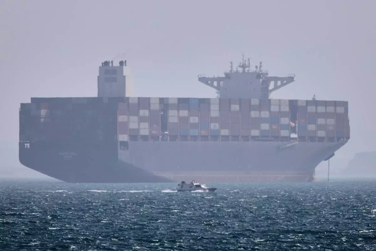 A container ship sits at anchor as a small motorboat passes in the foreground in the Strait of Hormuz off Bandar Abbas, Iran, Saturday, May 2, 2026. (Amirhosein Khorgooi/ISNA via AP)