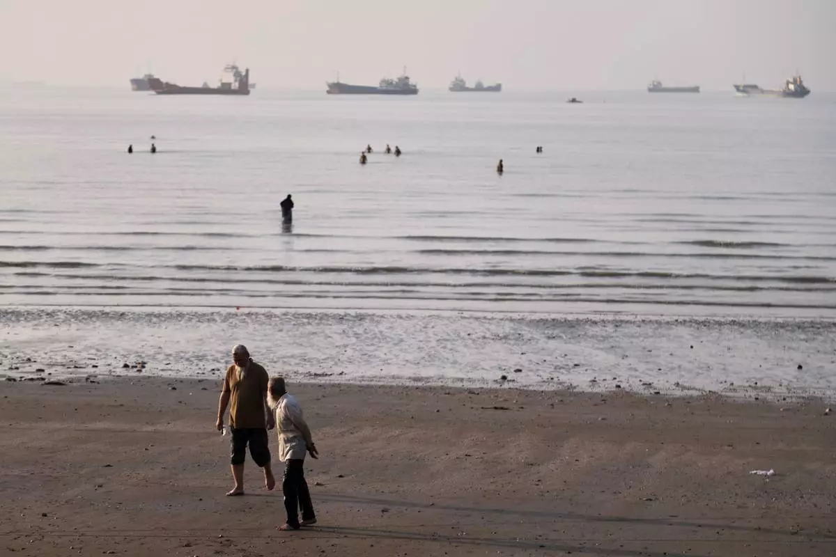 Men walk on the shoreline as people wade in the water in the Strait of Hormuz, where cargo and service vessels are anchored off Bandar Abbas, Iran, Monday, June 1, 2026. (Amirhosein Khorgooi/ISNA via AP)