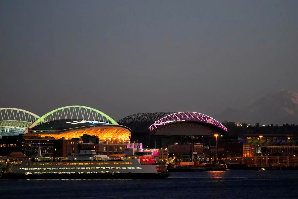 FILE - A Washington State ferry comes in to dock at the Seattle ferry terminal in front of Lumen Field, left, and T-Mobile Park, right, with Mount Rainier visible at right, as the sun sets Oct. 29, 2023, in Seattle. (AP Photo/Lindsey Wasson, File)