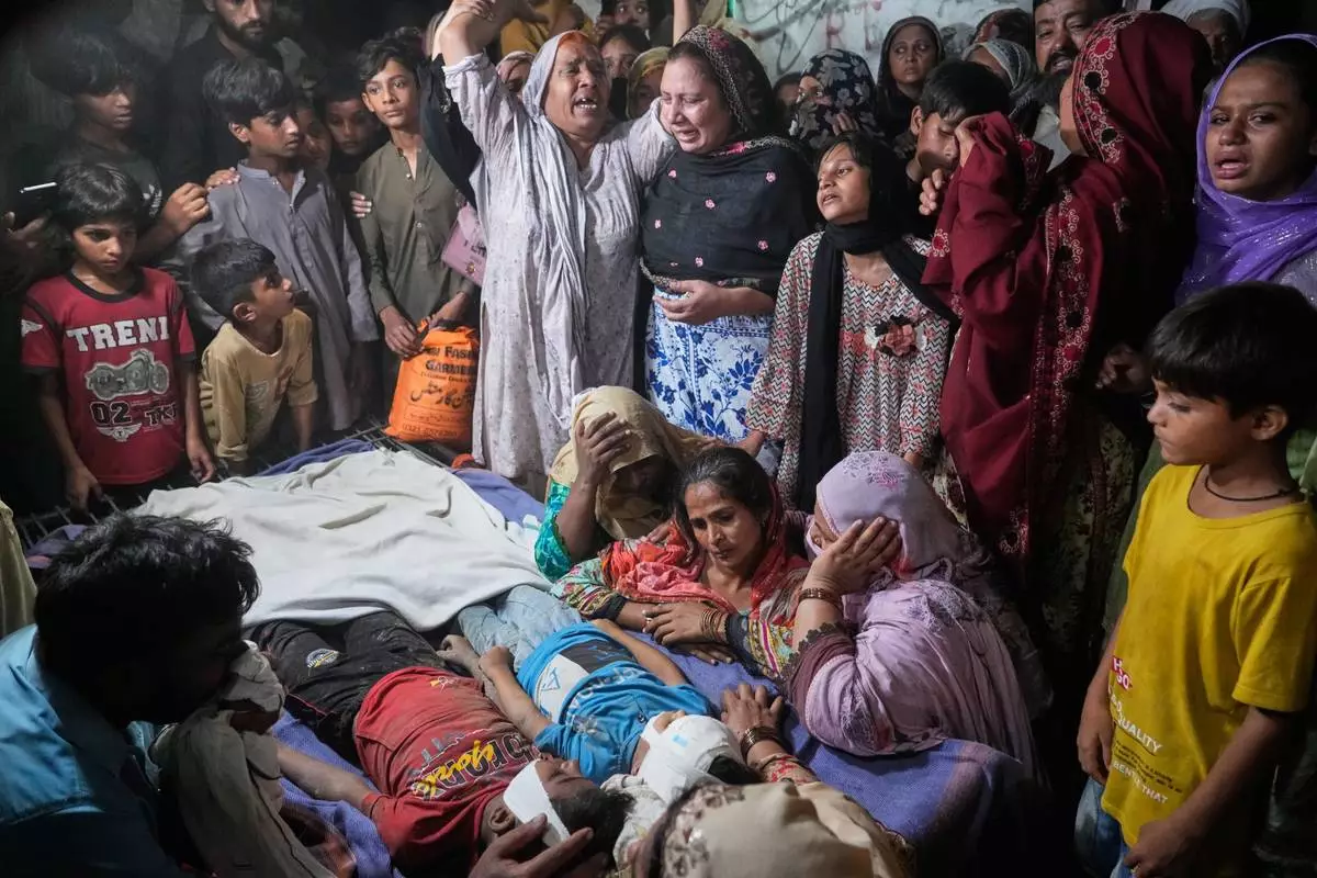 Women mourn next to the bodies of their children killed after the roof of a tutoring center under-construction collapsed, on the outskirts of Lahore, Pakistan, Tuesday, June 30, 2026. (AP Photo/K.M Chaudary)