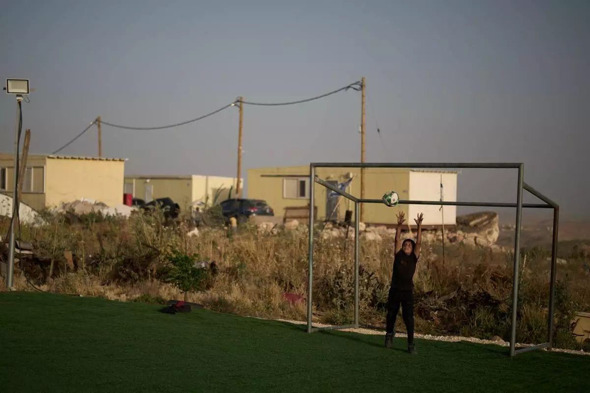Backdropped by caravans from the Israeli settlement of Carmel, a Palestinian boy jumps for a ball while playing goalkeeper at a small soccer pitch in the West Bank Bedouin village of Umm al-Khair, Tuesday, May 12, 2026. (AP Photo/Leo Correa)