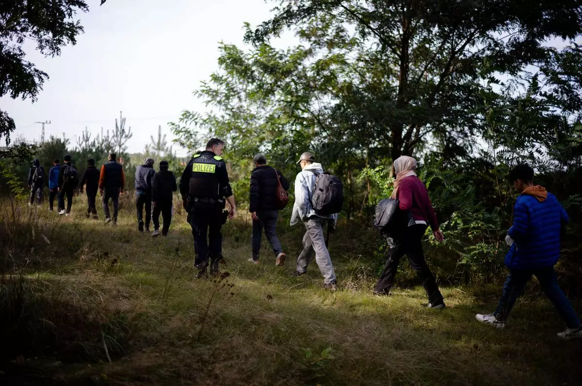 FILE - A Federal Police officer escorts a group of migrants who illegally crossed the border from Poland into Germany during a patrol in a forest near Forst, southeast of Berlin, Germany, on Oct. 11, 2023. (AP Photo/Markus Schreiber, File)