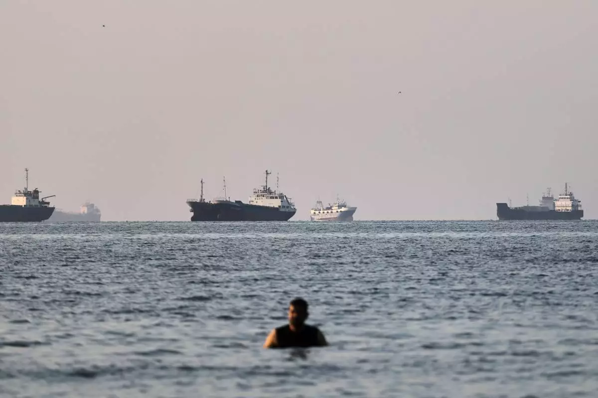 A person stands in shallow water as cargo and commercial vessels are anchored in the Strait of Hormuz off Bandar Abbas, Iran, Monday, June 8, 2026. (Amirhosein Khorgooi/ISNA via AP)
