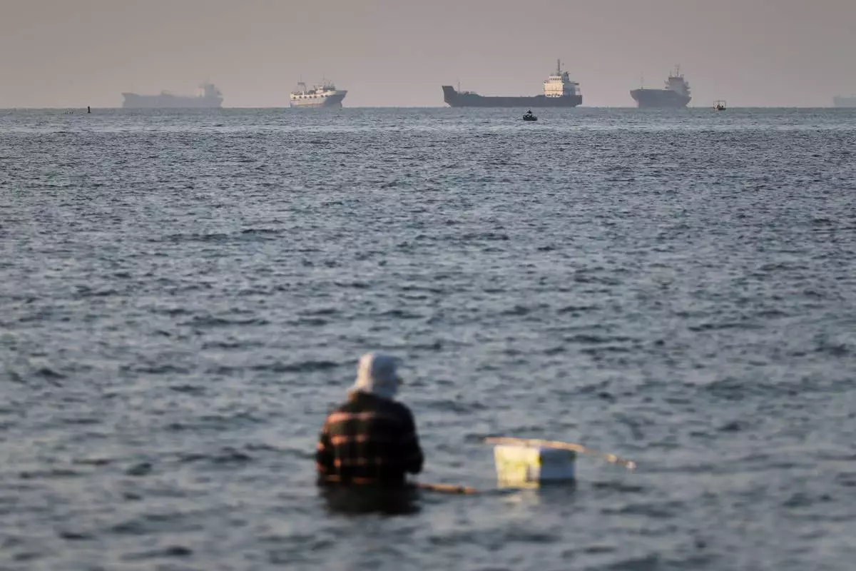 A person sits in shallow water as cargo and commercial vessels are anchored in the Strait of Hormuz off Bandar Abbas, Iran, Monday, June 8, 2026. (Amirhosein Khorgooi/ISNA via AP)