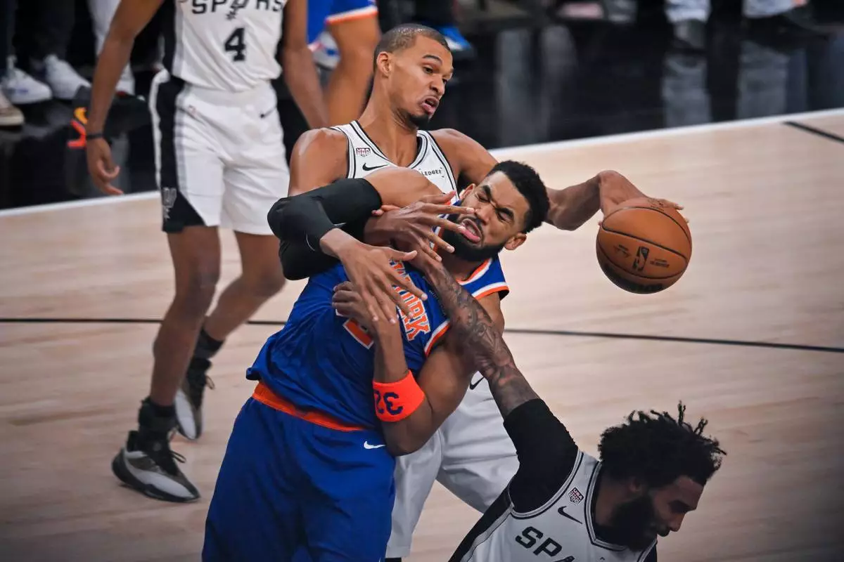 San Antonio Spurs forward Victor Wembanyama knocks the ball away from New York Knicks center Karl-Anthony Towns, center, during the first half of Game 5 of the NBA Finals basketball series, Saturday, June 13, 2026, in San Antonio. (AP Photo/Darren Abate)