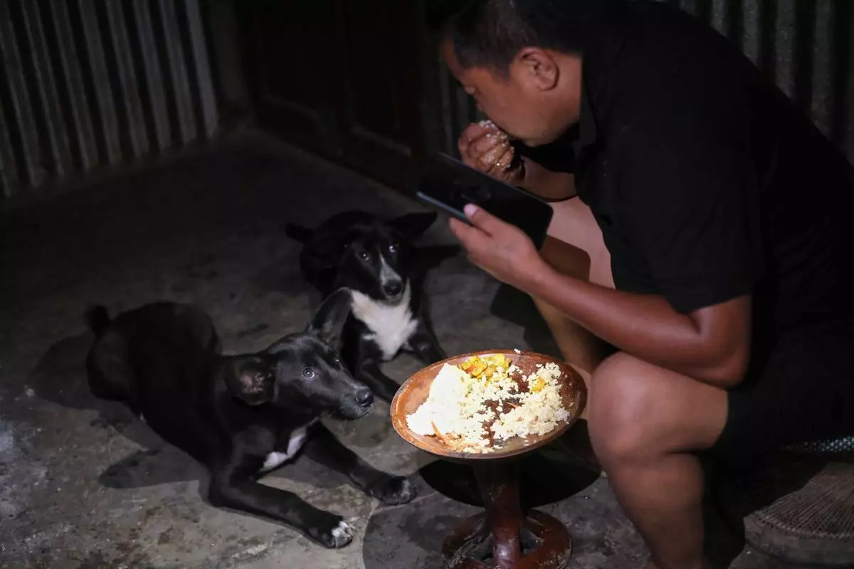 Tovi Murru, 32, eats dinner watched by his dogs inside their kitchen in Kohima, capital of the northeastern Indian state of Nagaland, Monday, July 6, 2026. (AP Photo/Yirmiyan Arthur)