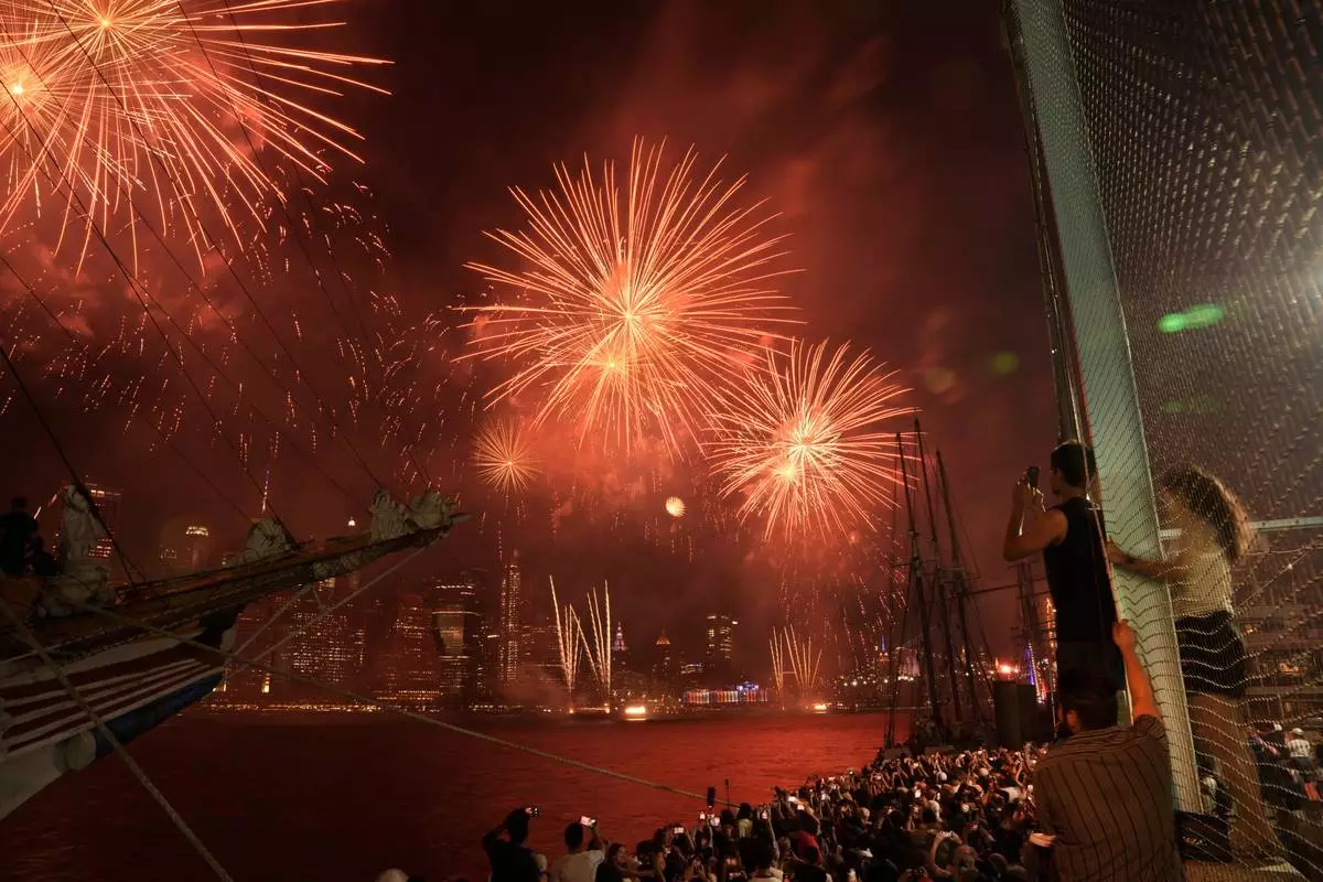 People watch fireworks explode over the New York City skyline as seen from the Brooklyn Borough of New York during the 4th of July celebration on Saturday, July 4, 2026. (AP Photo/Anna Connors)