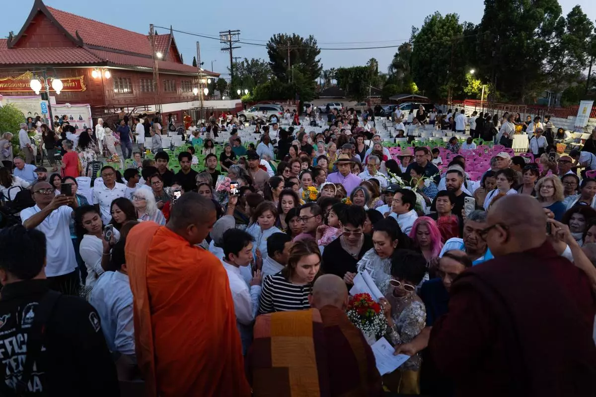 Bhikkhu Pannakara, bottom center, a Buddhist monk who led a Walk for Peace from Fort Worth, Texas, to Washington, D.C., hands out postcards and signs autographs for attendees at Wat Thai of Los Angeles in the North Hollywood section of Los Angeles, Monday, July 13, 2026. (AP Photo/Jae C. Hong)