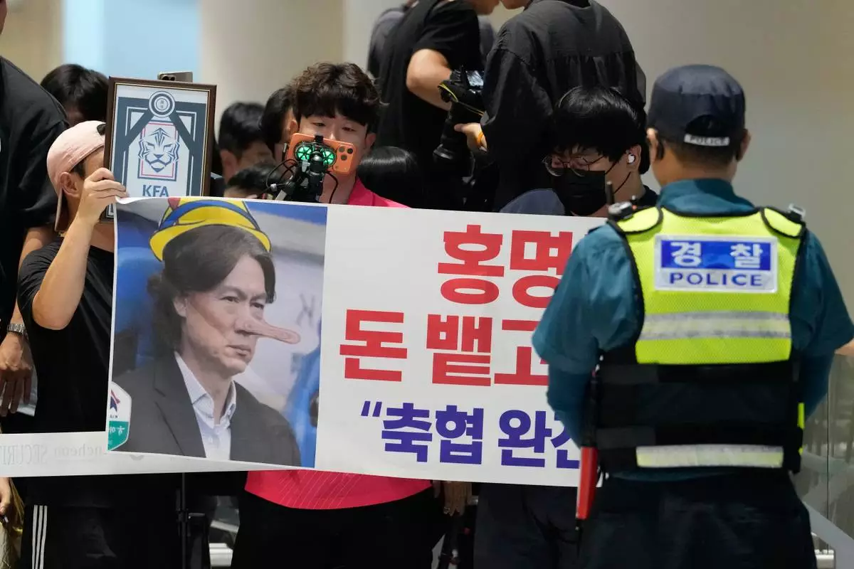Soccer fans hold a banner showing an image of South Korea's soccer head coach Hong Myung-bo, who has resigned, as they wait for his arrival following the team's early elimination from the World Cup soccer tournament, at the Incheon International Airport in Incheon, South Korea, Tuesday, June 30, 2026. The signs read "Hong Myung-bo! Spit the money and get out! Dismantle Korea Football Association". (AP Photo/Ahn Young-joon)