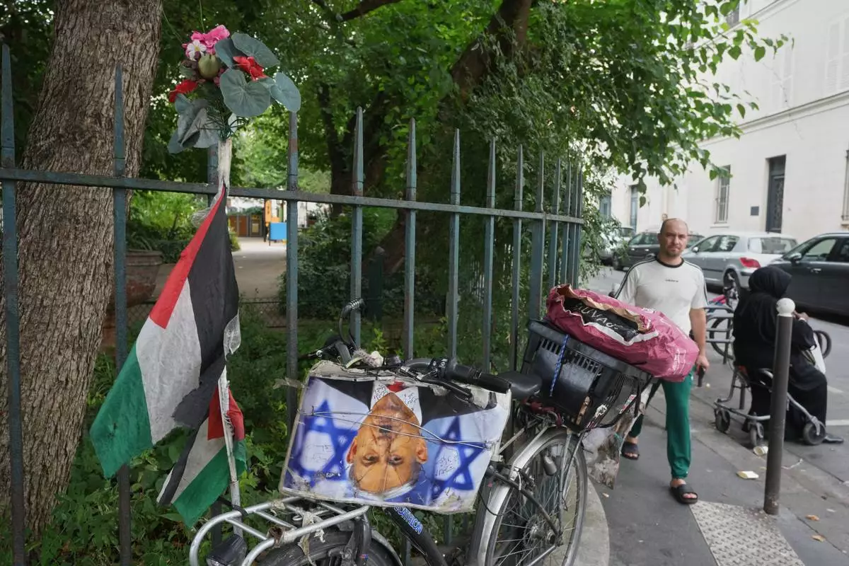 A man walks past a bicycle displaying a Palestinian flag and a photograph depicting Israeli Prime Minister Benjamin Netanyahu as Nazi dictator Adolf Hitler outside the Grand Mosque of Paris as it celebrates its 100th anniversary, Friday, July 17, 2026. (AP Photo/Michel Euler)