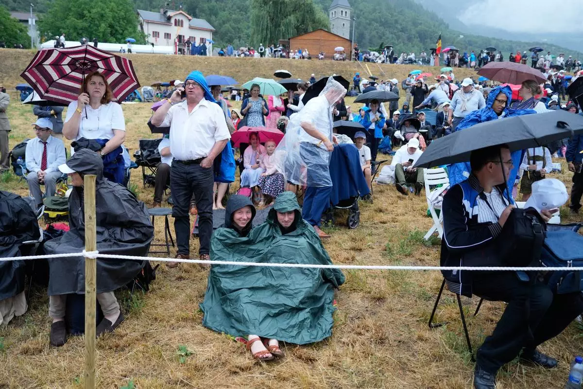 Faithful wait for the start of a consecration ceremony for four new bishops, outside a tent set up outside the Society of St. Pius X seminary, in Econe, Switzerland, Wednesday, July 1, 2026. (AP Photo/Baz Ratner)