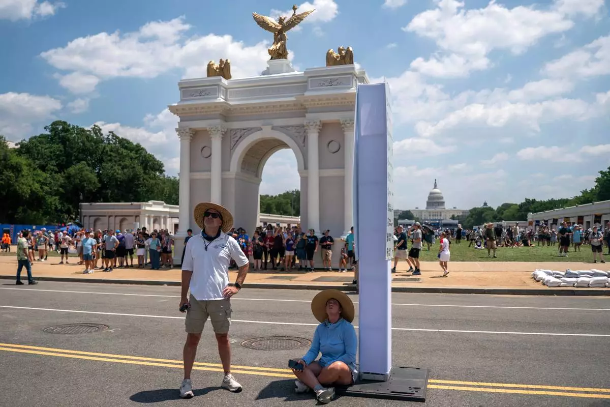 Attendees rest in the shade shortly before the event was closed for the afternoon due to extreme heat on the National Mall, Friday, July 3, 2026, in Washington. (AP Photo/Nathan Howard)