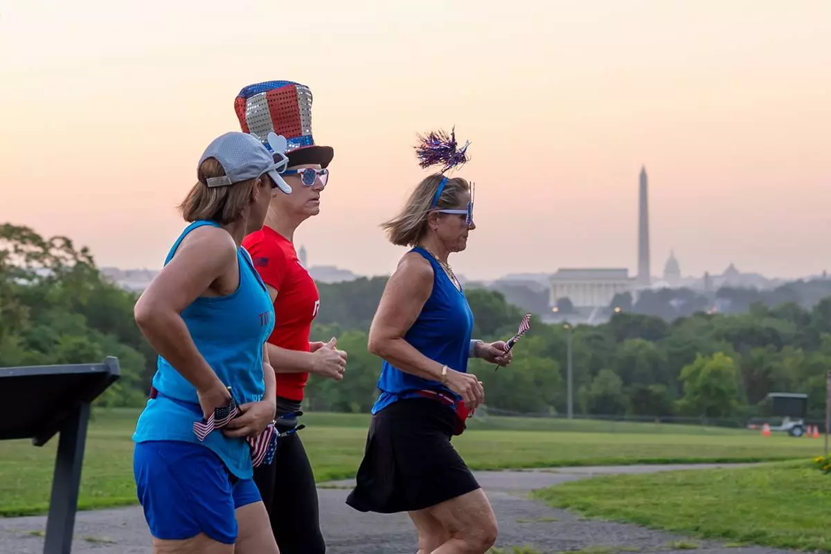 Runners wearing Independence Day-themed items jog at dawn past an overlook in Arlington, Va., as Washington prepares for sweltering temperatures, Friday, July 3, 2026. (AP Photo/J. Scott Applewhite)