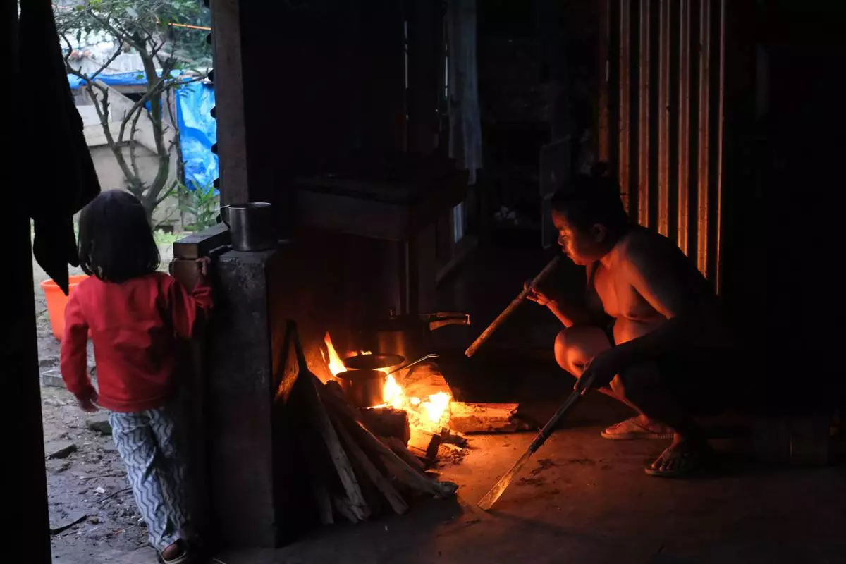 Tovi Murru, 32, blows into the fire to fan the flames, with his daughter Azatina, 3, by his side in Kohima, capital of the northeastern Indian state of Nagaland, Monday, July 6, 2026. (AP Photo/Yirmiyan Arthur)