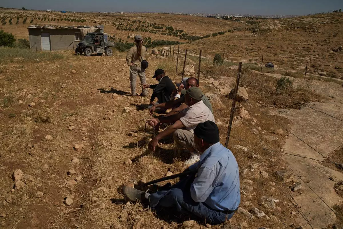 After Israeli soldiers told them to remain by the fence, Palestinians and an Israeli activist sit watching as settlers arrive in a vehicle after the settlers accused a local Palestinian resident of setting fire to a field, near the West Bank village of Susya in the Masafer Yatta region, Thursday, June 18, 2026. (AP Photo/Leo Correa)
