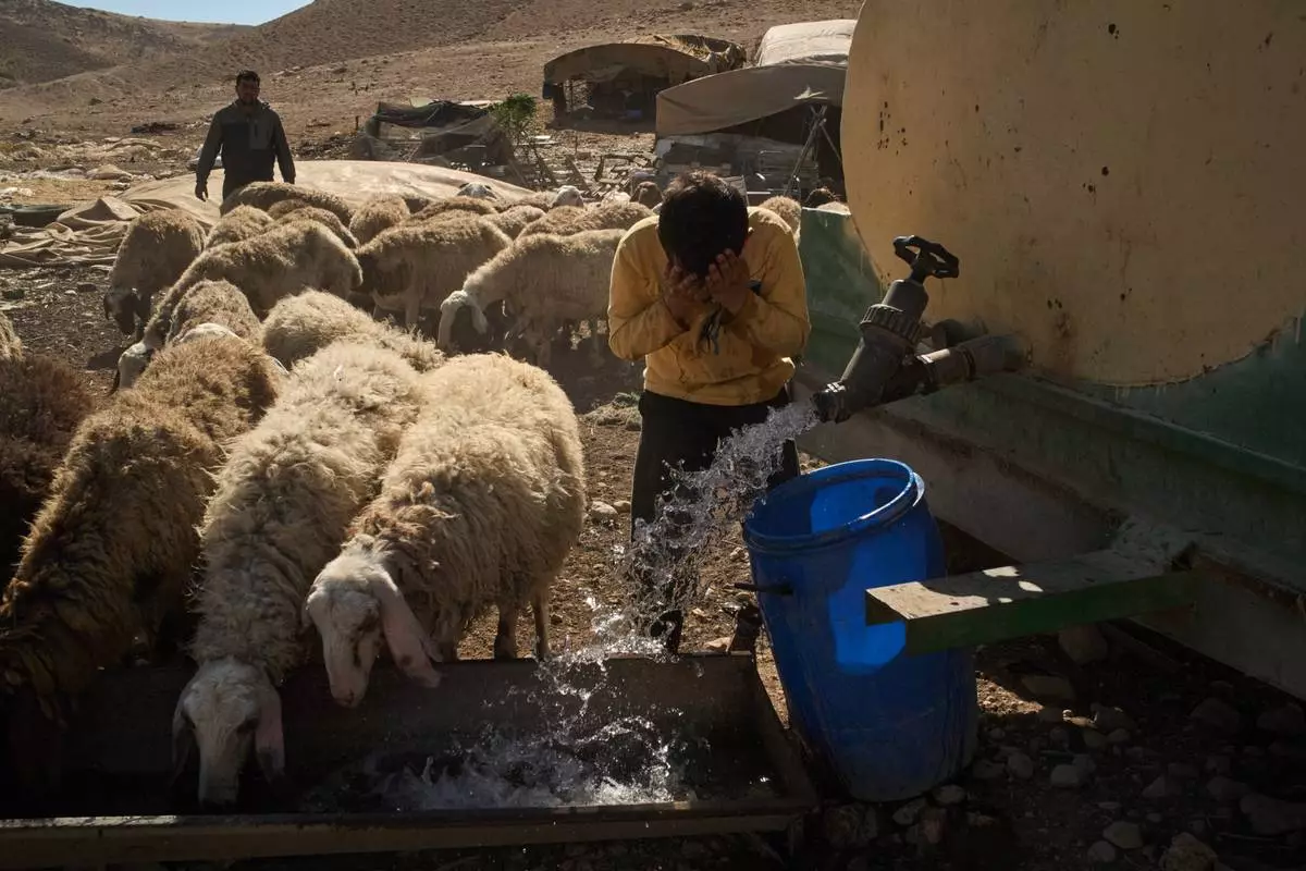 Hamoudi, 10, washes his face as he gives water to his family's sheep at a Palestinian community in the northern Jordan Valley in the occupied West Bank, Tuesday, June 23, 2026. (AP Photo/Leo Correa)
