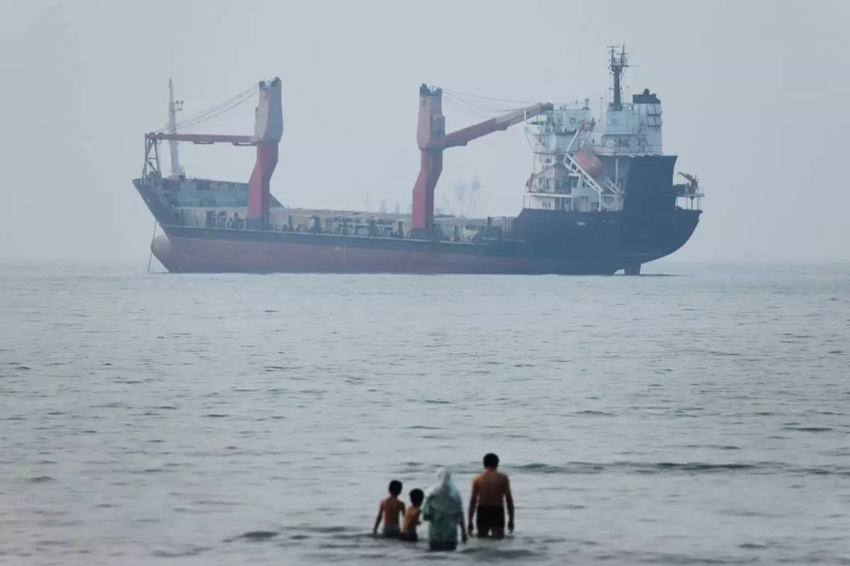 A group of people stands in shallow water as a cargo ship appears anchored in the Strait of Hormuz off Bandar Abbas, Iran, Tuesday, June 30, 2026. (Amirhosein Khorgooi/ISNA via AP)