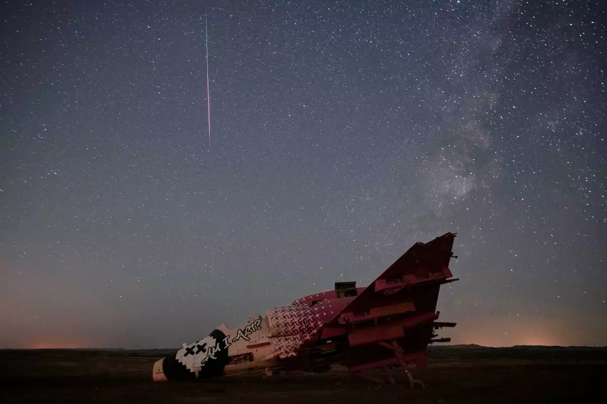 A meteor streaks above a destroyed aircraft used for training purposes in the Negev Desert, Israel, Thursday, Aug. 13, 2026. (AP Photo/Ohad Zwigenberg)