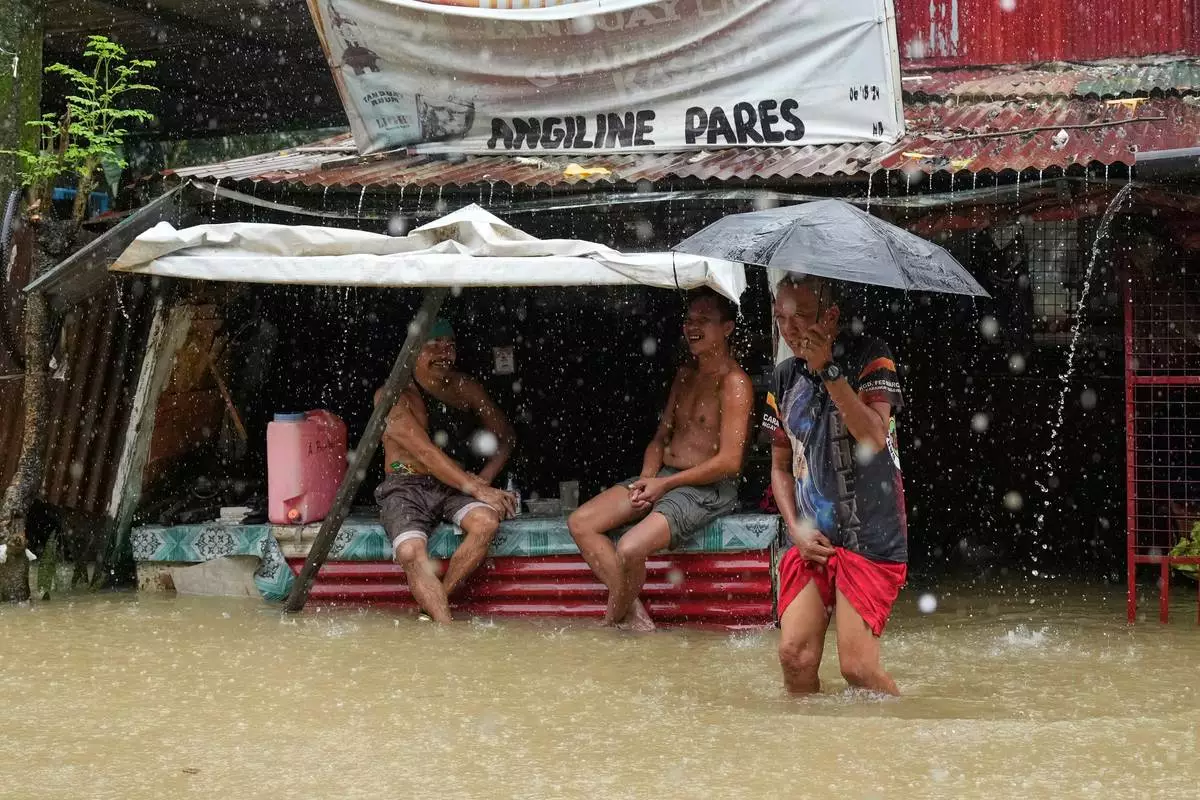 Residents stay at a store along floodwaters caused by heavy seasonal monsoon rains at Bagong Silangan village in Quezon city, Metro Manila, Philippines, Monday, Aug. 10, 2026. (AP Photo/Aaron Favila)