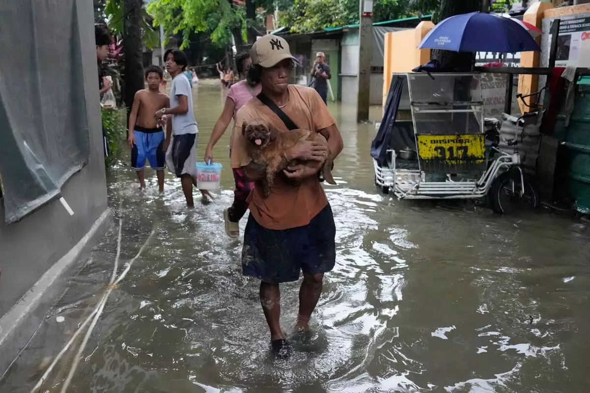 A man carries his dog along floodwaters caused by heavy seasonal monsoon rains at Bagong Silangan village in Quezon city, Metro Manila, Philippines Monday, Aug. 10, 2026. (AP Photo/Aaron Favila) CORRECTION: Corrects typo in location to Silangan, instead of Silagan