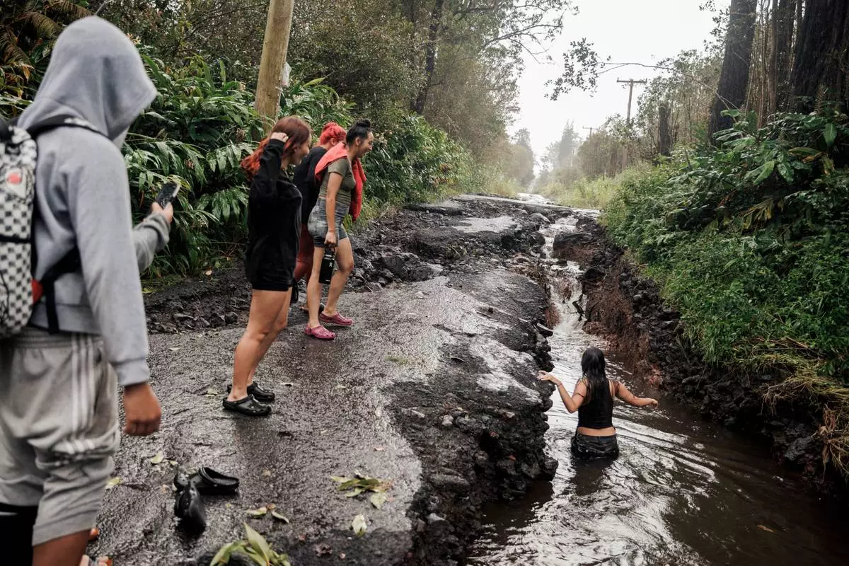 A teenager wades through a pool of water in a washed-out section of a damaged road in Mountain View, Hawaii, Sunday, Aug. 16, 2026, after a severe weather system went through the area. (Stephen Lam/San Francisco Chronicle via AP)