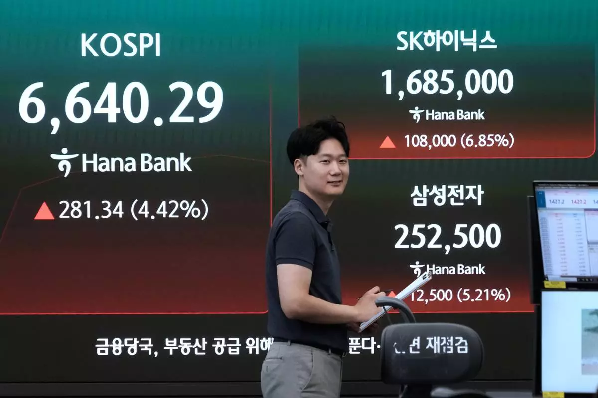 A currency trader passes by a screen showing the Korea Composite Stock Price Index (KOSPI), SK Hynix and Samsung Electronics Co. stock price at the foreign exchange dealing room of the Hana Bank headquarters in Seoul, South Korea, Wednesday, Aug. 5, 2026. (AP Photo/Ahn Young-joon)