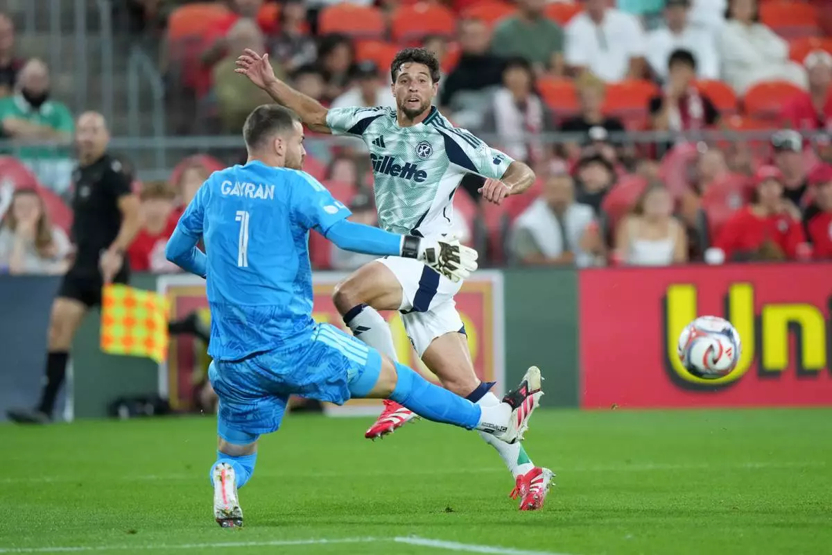 New England Revolution defense Matt Polster (8) watches his shot as Toronto FC goalkeeper Luka Gavran (1) gets a piece of the ball to deflect from the net during the second half of an MLS soccer game in Toronto, Saturday, Aug. 15, 2026. (Nathan Denette/The Canadian Press via AP)