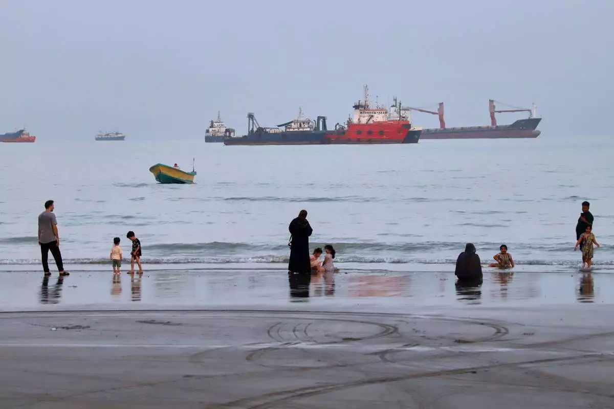 People spend time at a beach as commercial vessels are anchored in the Strait of Hormuz off Bandar Abbas, Iran, Wednesday, Aug. 5, 2026. (Amirhosein Khorgooi/ISNA via AP)