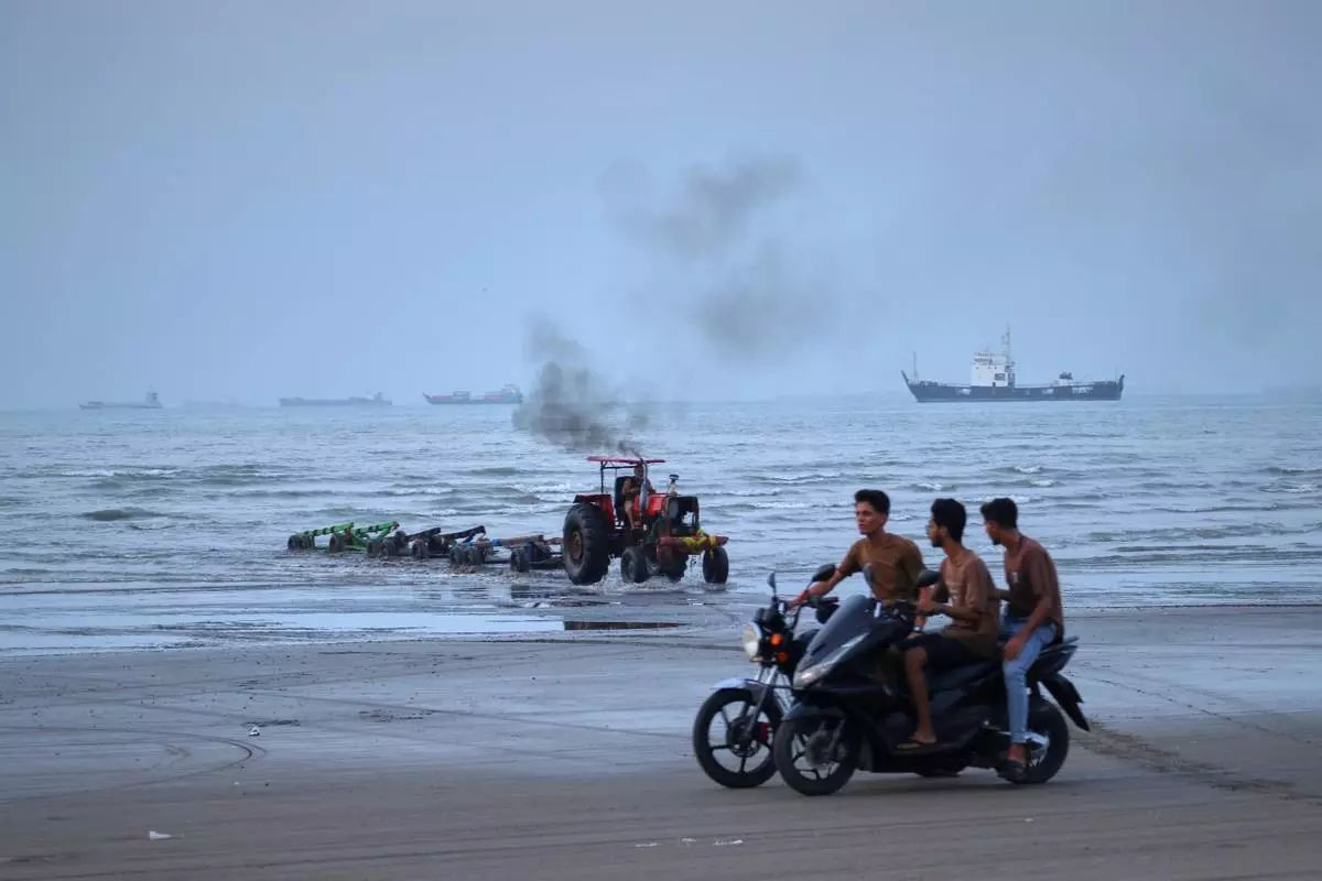 Young men ride motorcycles along the shore as a tractor pulls equipment from the water and commercial vessels appear anchored in the Strait of Hormuz off Bandar Abbas, Iran, Monday, July 27, 2026. (Razieh Poudat/ISNA via AP)