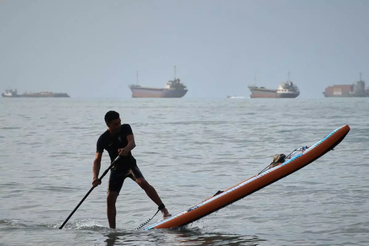 A man paddles a stand-up paddleboard as cargo ships and other commercial vessels appear anchored in the Strait of Hormuz off Bandar Abbas, Iran, Monday, July 27, 2026. (Razieh Poudat/ISNA via AP)
