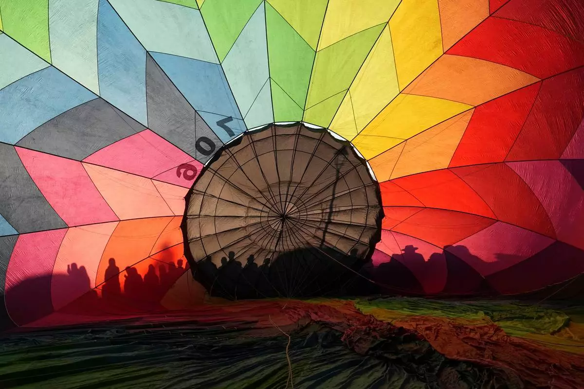 People's shadows are cast on a hot air balloon's envelope during the 5th edition of the Middle of the World International Hot Air Balloon Festival in Quito, Ecuador, Friday, Aug. 21, 2026. (AP Photo/Dolores Ochoa)