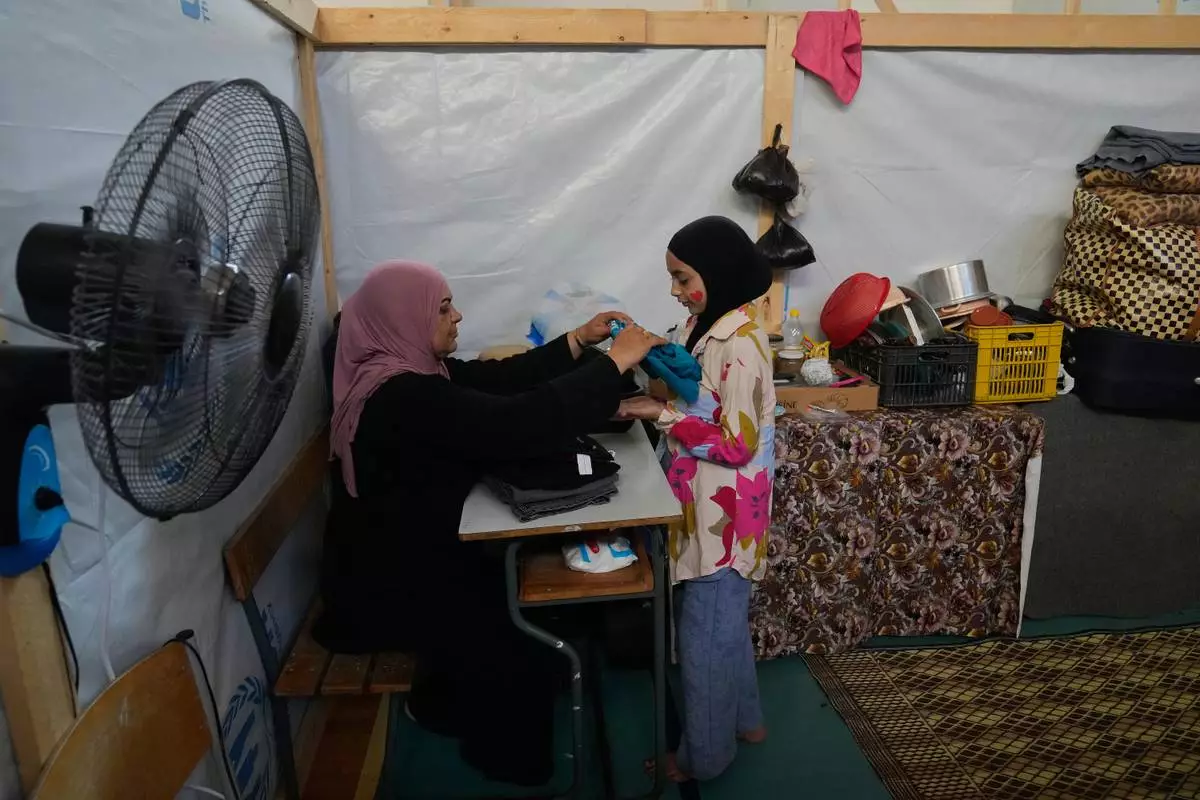 Displaced Randa al-Taki, 51, and her daughter Fatima Khashab, 11, arrange their clothes inside a makeshift room that was set on a basketball court inside a public school turned into a shelter for people whose villages in southern Lebanon were destroyed or occupied by Israeli forces, in Tyre, southern Lebanon, Thursday, Aug. 27, 2026. (AP Photo/Hussein Malla) CORRECTION: Last name corrected to Khashab, instead of Haidar