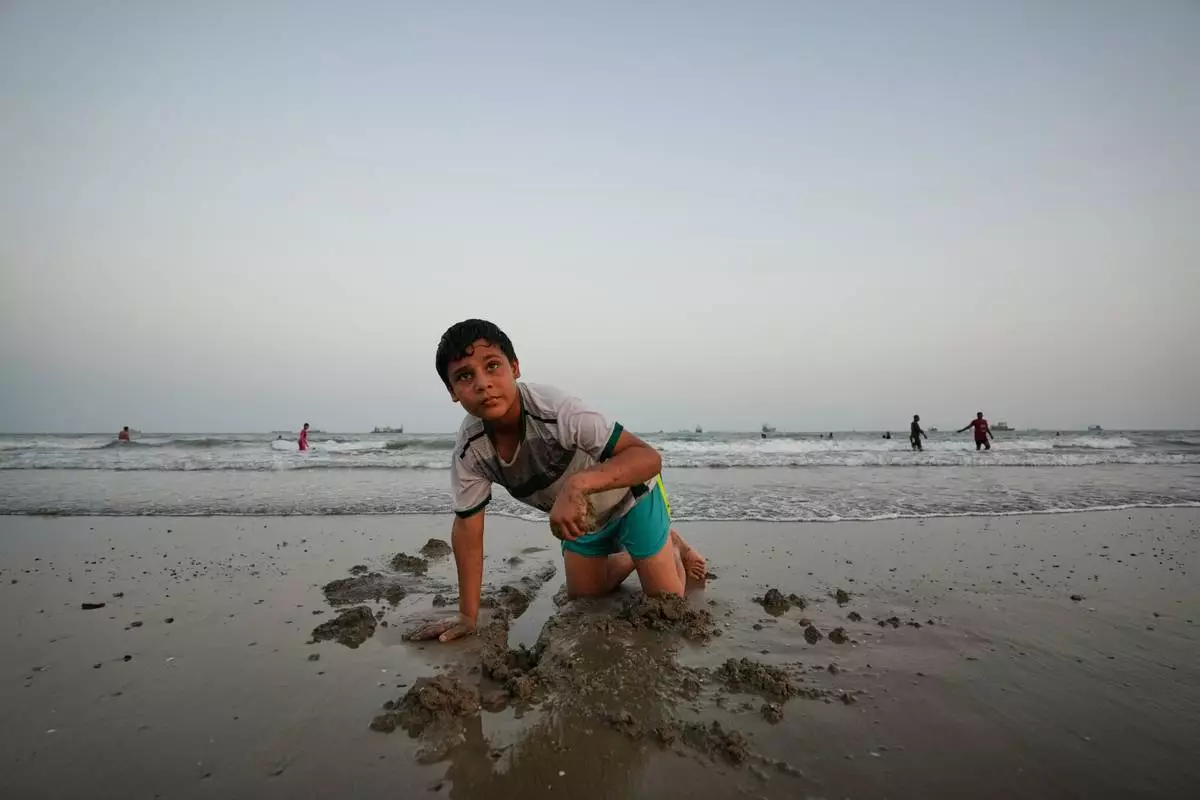 A boy plays in wet sand as others swim and commercial vessels lie anchored in the Strait of Hormuz off Bandar Abbas, Iran, Friday, Sept. 4, 2026. (AP Photo/Vahid Salemi)