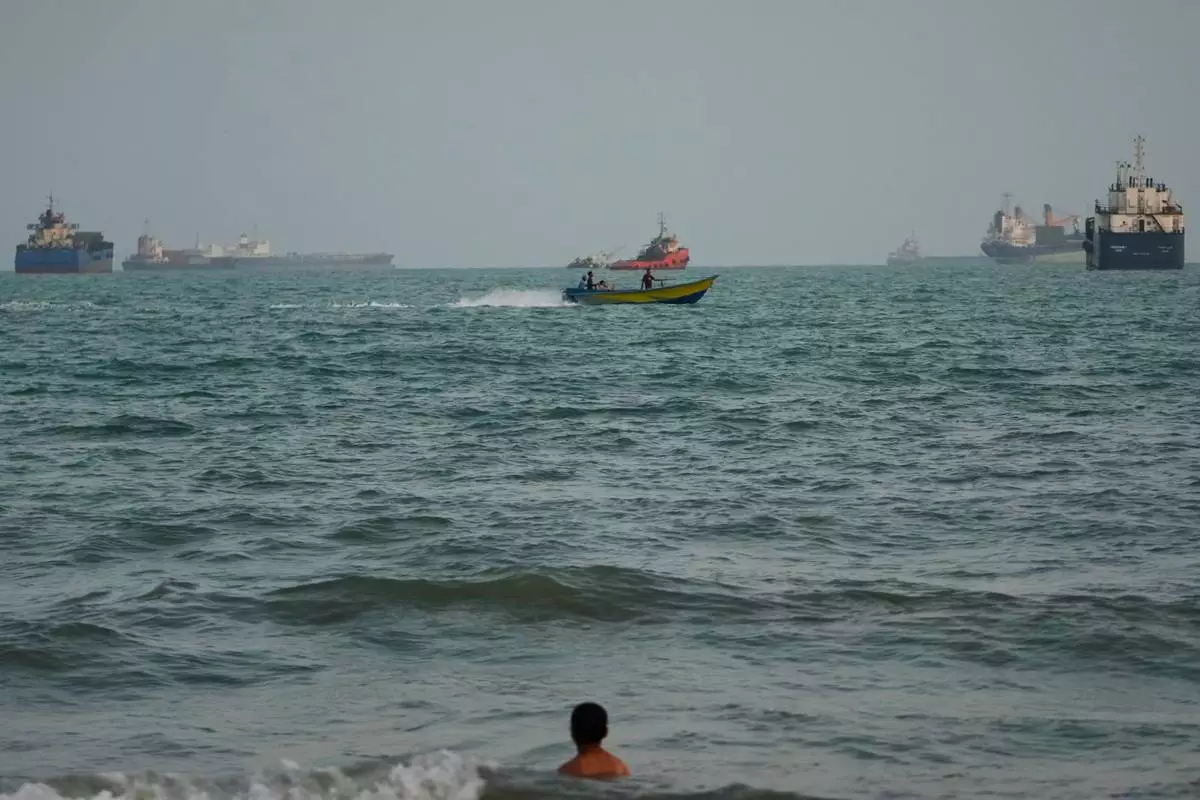 A swimmer remains near the shore as a motorboat passes commercial vessels anchored in the Strait of Hormuz off Bandar Abbas, Iran, Friday, Sept. 4, 2026. (AP Photo/Vahid Salemi)