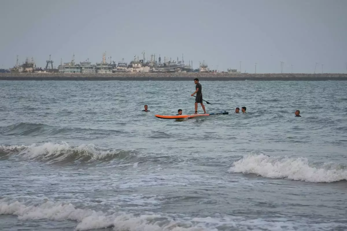 A man paddleboards among swimmers in the Strait of Hormuz, with boats docked at a harbor in Bandar Abbas, Iran, Friday, Sept. 4, 2026. (AP Photo/Vahid Salemi)