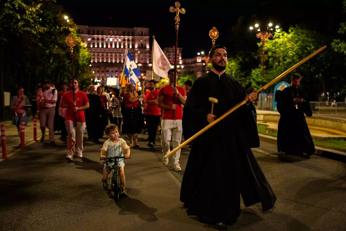 A child rides a bicycle next to priests leading the Procession of Lights, part of a four-day program of the International Meeting of Orthodox Youth (ITO), in Bucharest, Romania, Wednesday, Sept. 2, 2026. (AP Photo/Andreea Alexandru)