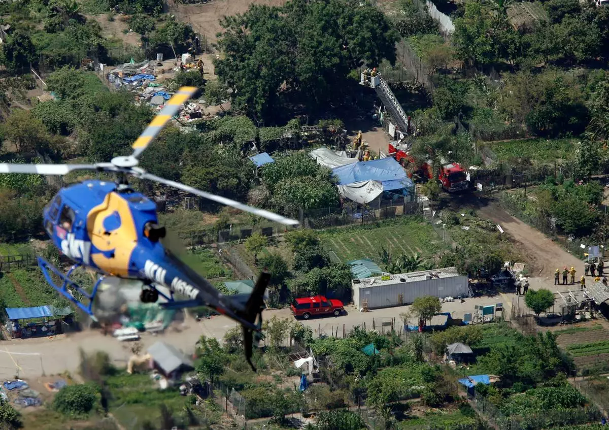 FILE - A news helicopter flies over the South Central urban community garden in downtown Los Angeles, June 13, 2006, as authorities use a Los Angeles Fire Department ladder truck ladder, upper right, to extract actress Daryl Hannah and tree sitter John Quigley from a walnut tree. (AP Photo/Damian Dovarganes, File)