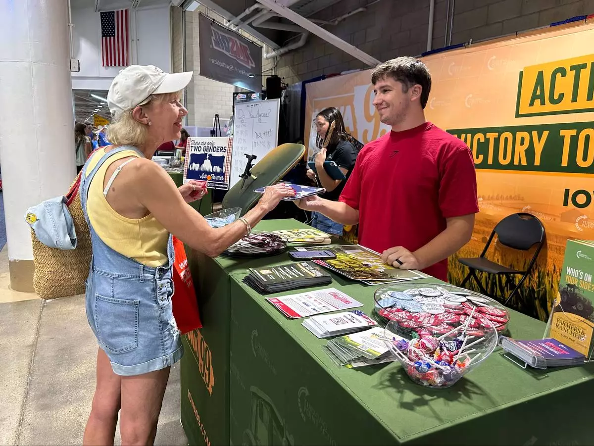 A Turning Point Action staffer gives an American flag to a voter at the Iowa State Fair in Des Moines, Iowa, Friday, Aug. 21, 2026. (AP Photo / Hannah Fingerhut)
