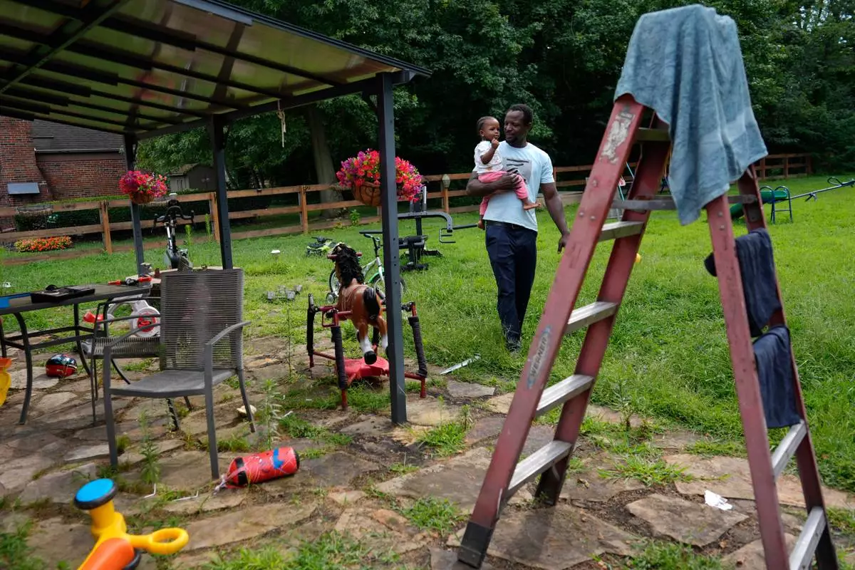 Khalidou Sy, a Mauritanian immigrant, carries his young daughter in the backyard of the family's home in Lockland, Ohio, Friday, July 31, 2026. (AP Photo/Carolyn Kaster)