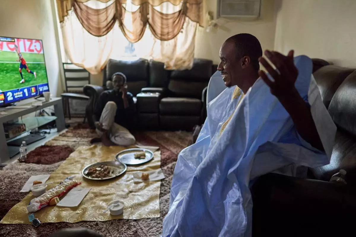 Samba Diallo, right, wears his daraa, a traditional robe worn in his homeland, Mauritania, after eating a communal meal of lamb and bread on the floor of his apartment with his roommate, Alassane Sow, in Lockland, Ohio, Friday, July 17, 2026. Diallo is part of an unprecedented migration surge, and an Associated Press analysis of exclusive data shows they turned some of the unlikeliest of places, like Lockland, into new American melting pots. (AP Photo/Carolyn Kaster)