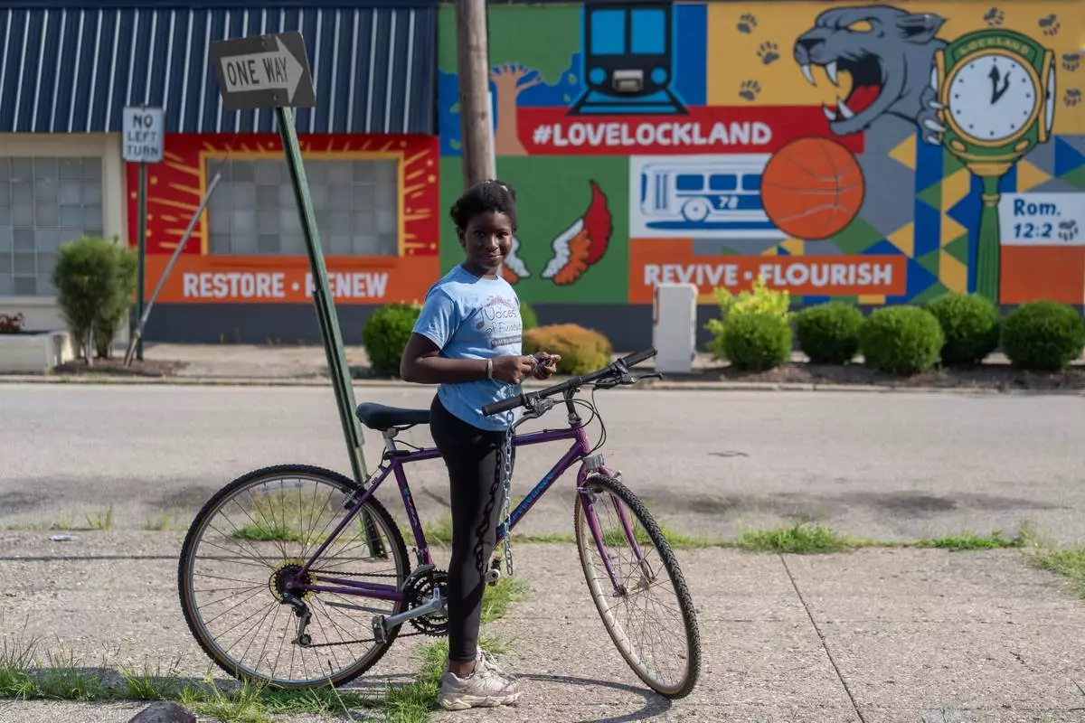 Halimata Ndiaye pauses on the new purple bike she just received from Bikes and Stuff in Lockland, Ohio, Friday, July 10, 2026. The shop offers free bikes to anyone willing to help refurbish one and has become the center of life for the West African community here. (AP Photo/Carolyn Kaster)