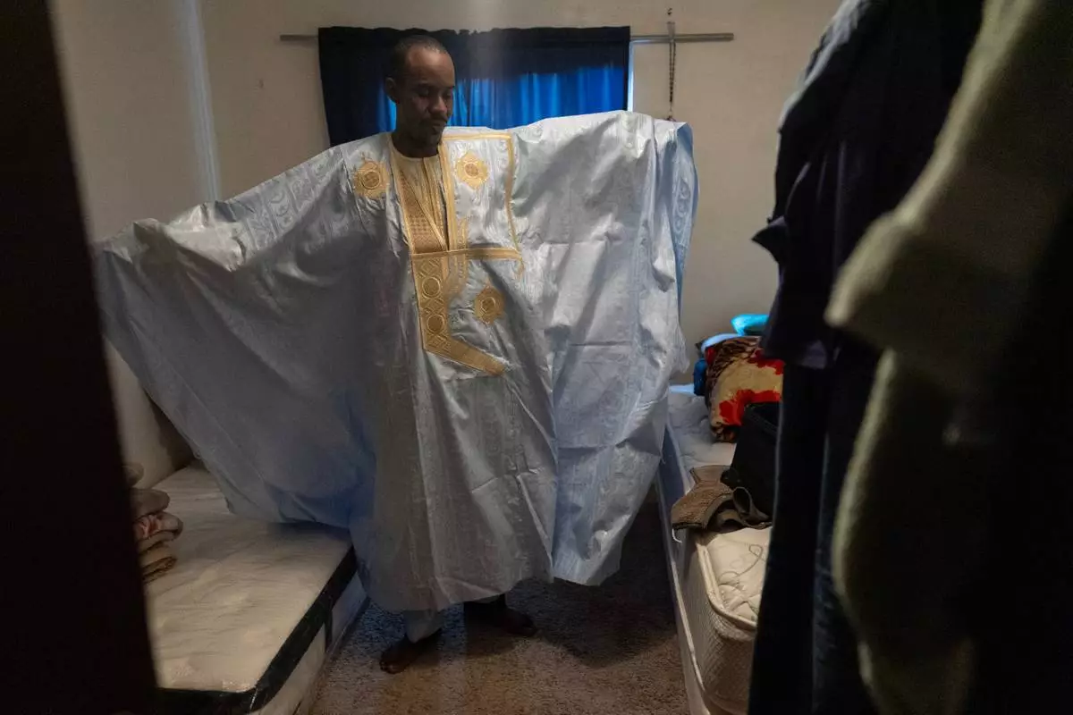 Samba Diallo displays his daraa, a loose-fitting traditional robe worn by men in Mauritania, as he stands in the bedroom of his shared apartment in Lockland, Ohio, Friday, July 17, 2026. Diallo, like many Mauritanians, spent weeks making his way through a half-dozen countries on buses, on foot, through the jungle and across rivers, until he finally walked across the U.S. southern border and asked for asylum. (AP Photo/Carolyn Kaster)