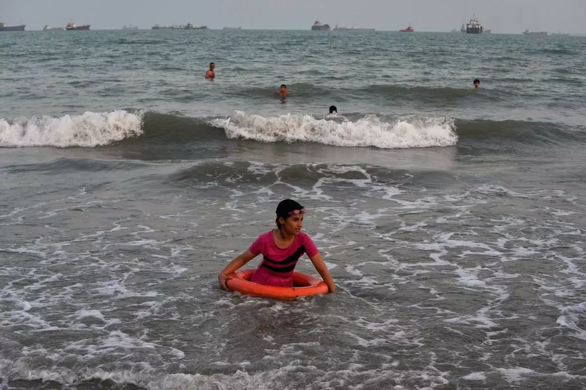 A girl plays in the water with a swim ring as commercial vessels lie anchored in the Strait of Hormuz off Bandar Abbas, Iran, Friday, Sept. 4, 2026. (AP Photo/Vahid Salemi)